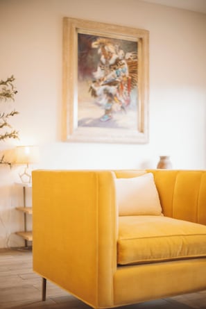 En gul sofa med en hvid pude i et rum med et billede på væggen.