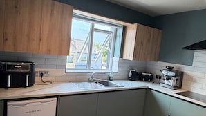A modern kitchen with a built-in dishwasher, a coffee machine, and a window providing natural light. - House Sleeps 8 With Parking and Balcony (Clones)