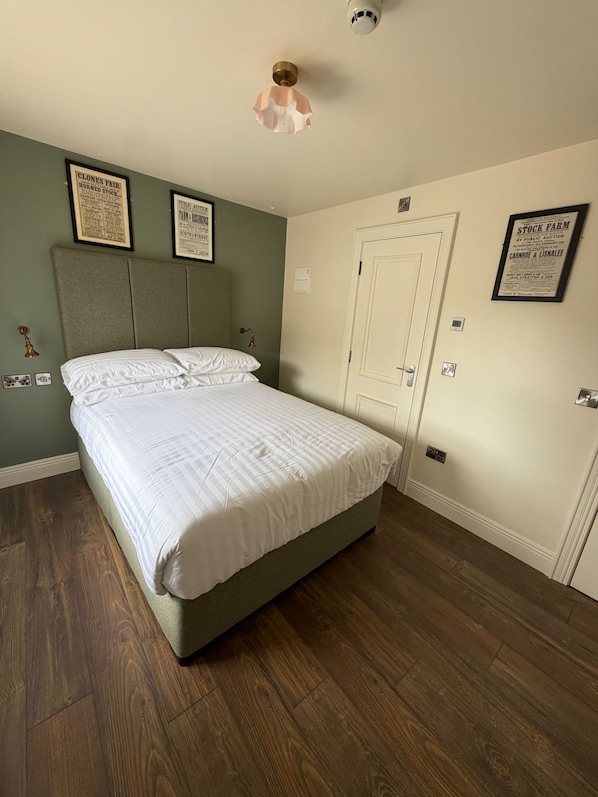 Quarto com cama, cabeceira, porta e certificados emoldurados na parede.