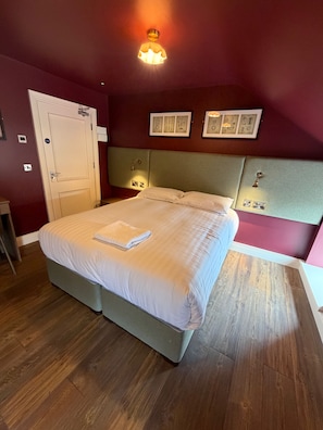 Cama bem arrumada com uma toalha dobrada, porta com uma placa e quadros na parede.