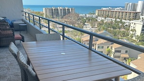 A balcony with a wooden table and wicker chairs, overlooking a coastal cityscape. - Siesta Key Penthouse with Expansive Ocean Views (Siesta Key)
