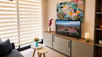 Una sala de estar moderna con un ventanal grande, un televisor de pantalla plana, un cuadro abstracto colorido y una mesita con un florero.