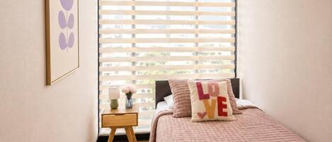 A bedroom with a bed, a nightstand, a window with blinds, and a wall-mounted picture.