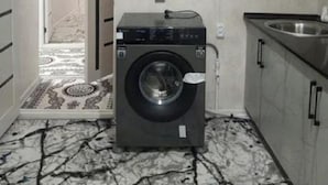 Un lavadero pequeño con lavadora, lavamanos y una puerta que da a un pasillo.