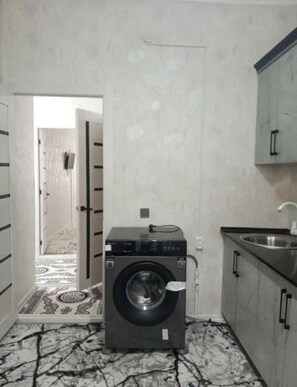 Lavanderia compacta com máquina de lavar, pia e porta para um corredor.