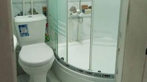 Un baño con inodoro, cabina de ducha con mampara de vidrio y piso de baldosas.