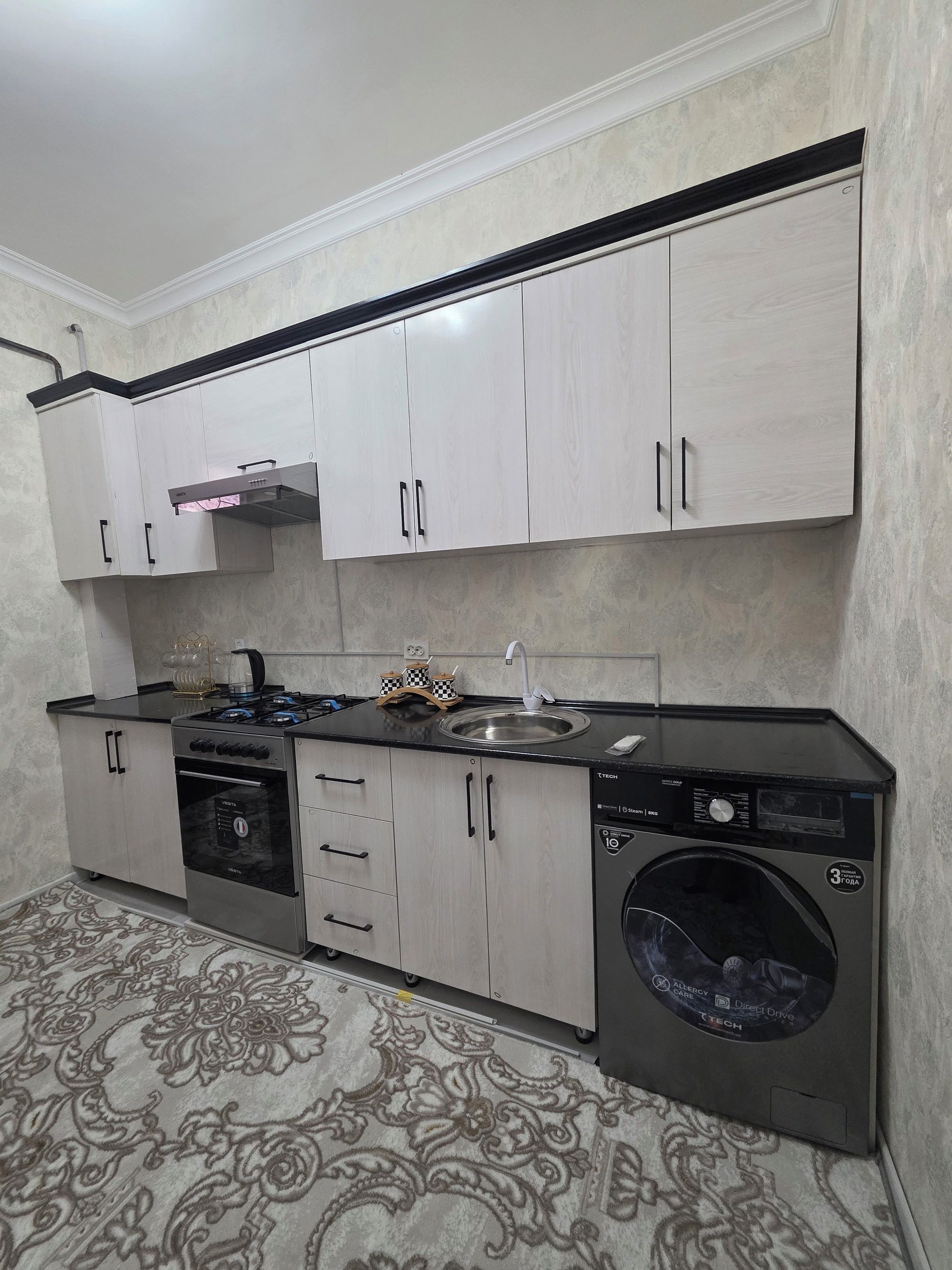 A compact kitchen with a gas stove, oven, sink, and a front-loading washing machine.