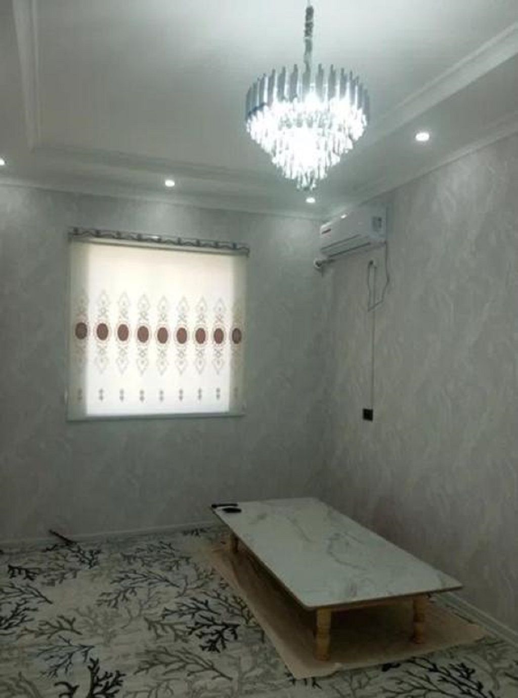 Una habitación con candelabro, una ventana con persianas decorativas y una cama con alfombra estampada.