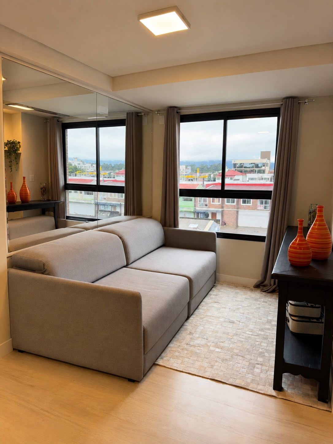A modern hotel room with a sofa, a small table, and a view of the city through large windows.