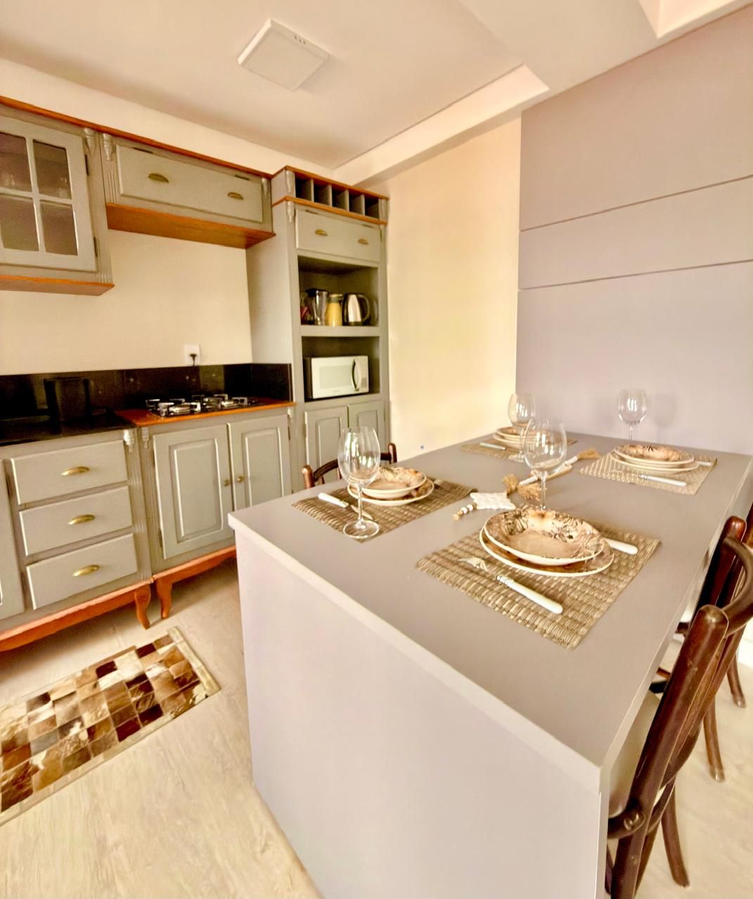 A modern kitchen with grey cabinets, a central island with a dining table set for four, and a built-in oven.