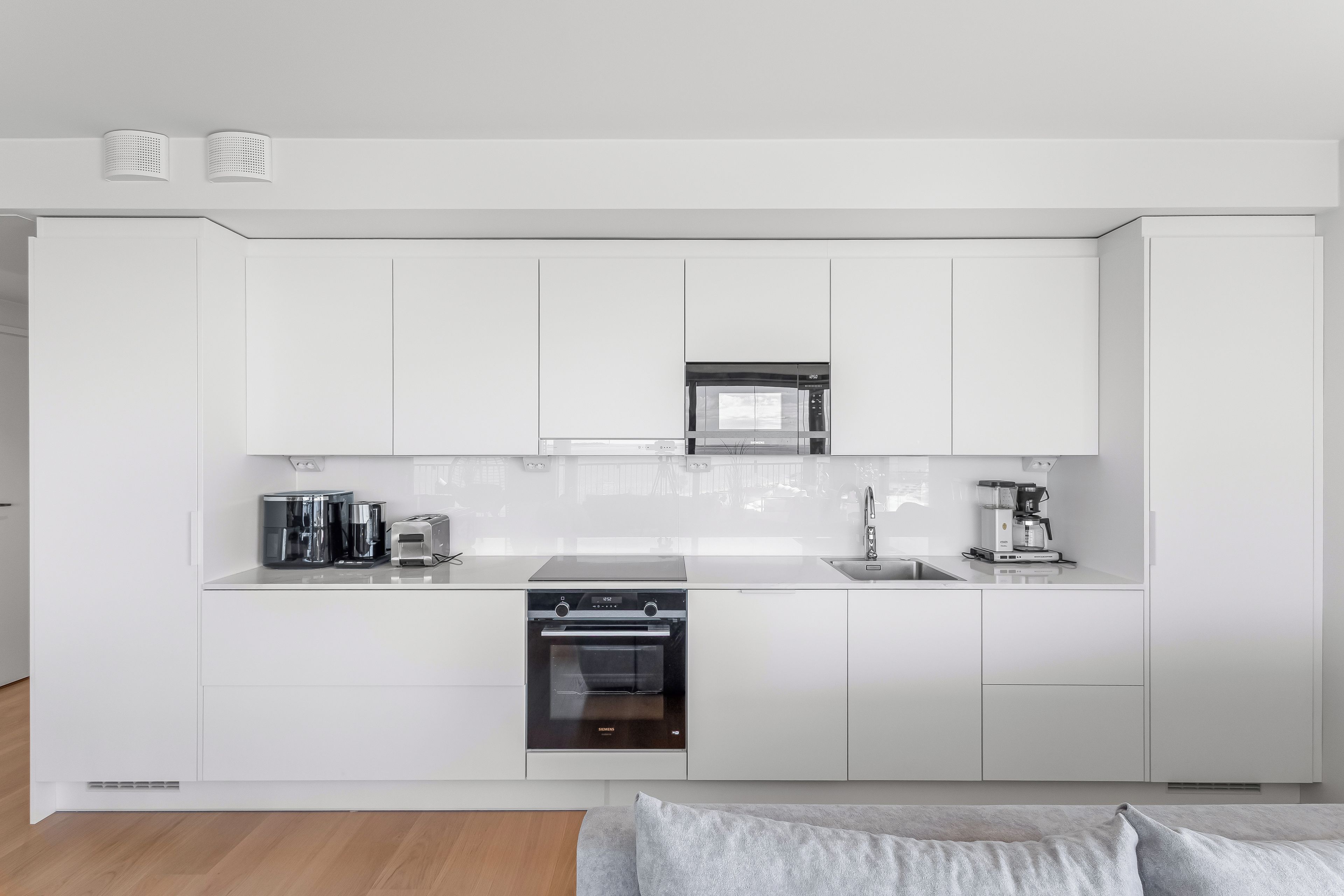 Une cuisine moderne avec des meubles blancs, un four à micro-ondes encastré, une machine à café et un four Siemens.