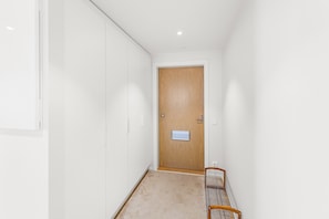 Un pasillo estrecho con una puerta de madera, un banco y una pared blanca.