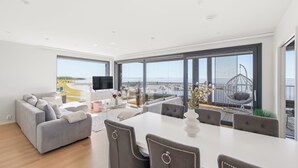 A modern living room with a sofa, dining table, and chairs, large windows with a view of the sea, and a balcony with outdoor seating. - Stunning beachfront apartment for 1-8 people in Oulu Pateniemenranta. (Oulu)