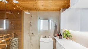 A modern bathroom with a glass shower enclosure, a white sink, and a wooden ceiling. - Stunning beachfront apartment for 1-8 people in Oulu Pateniemenranta. (Oulu)