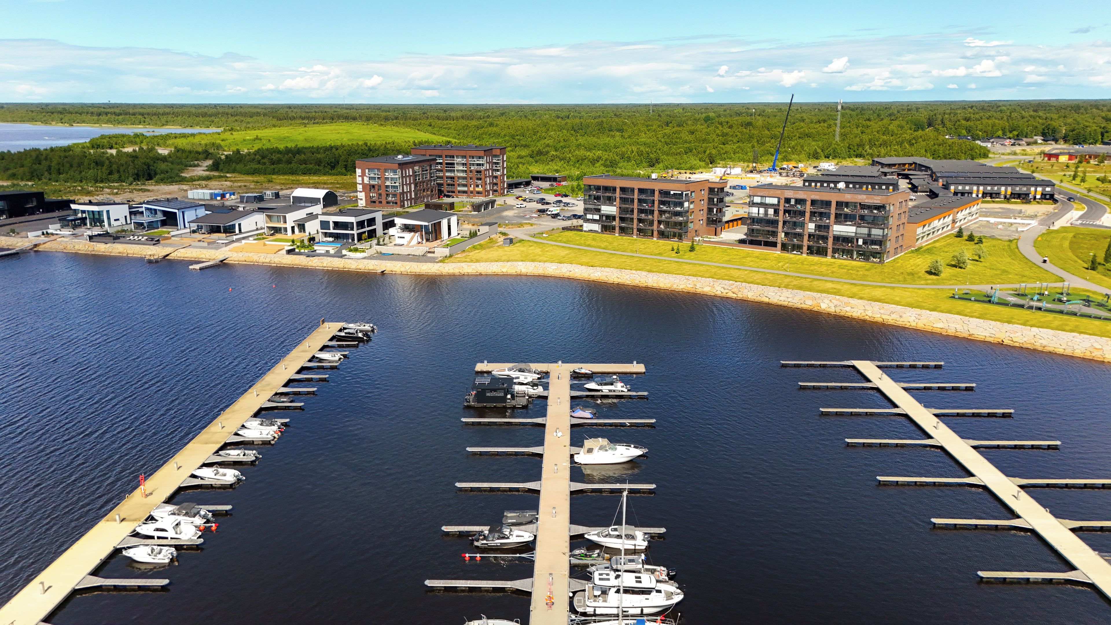 Un puerto deportivo con barcos amarrados, rodeado de edificios modernos y un paisaje boscoso.
