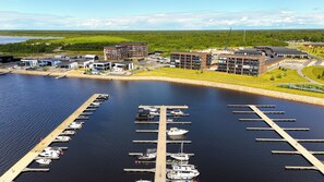 Un port de plaisance où sont amarrés des bateaux, entouré de bâtiments modernes et d’un paysage boisé.