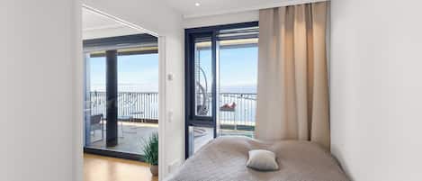 A modern bedroom with a large bed, a view of the sea, and a balcony with outdoor furniture.