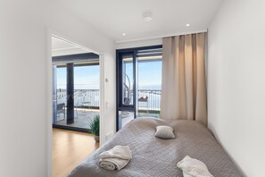 Un dormitori modern amb un llit gran, vistes al mar i un balcó amb mobles d'exterior.