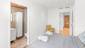 A modern bedroom with a bed, a chair, a wardrobe, and a bathroom visible through an open door. - Stunning beachfront apartment for 1-8 people in Oulu Pateniemenranta. (Oulu)