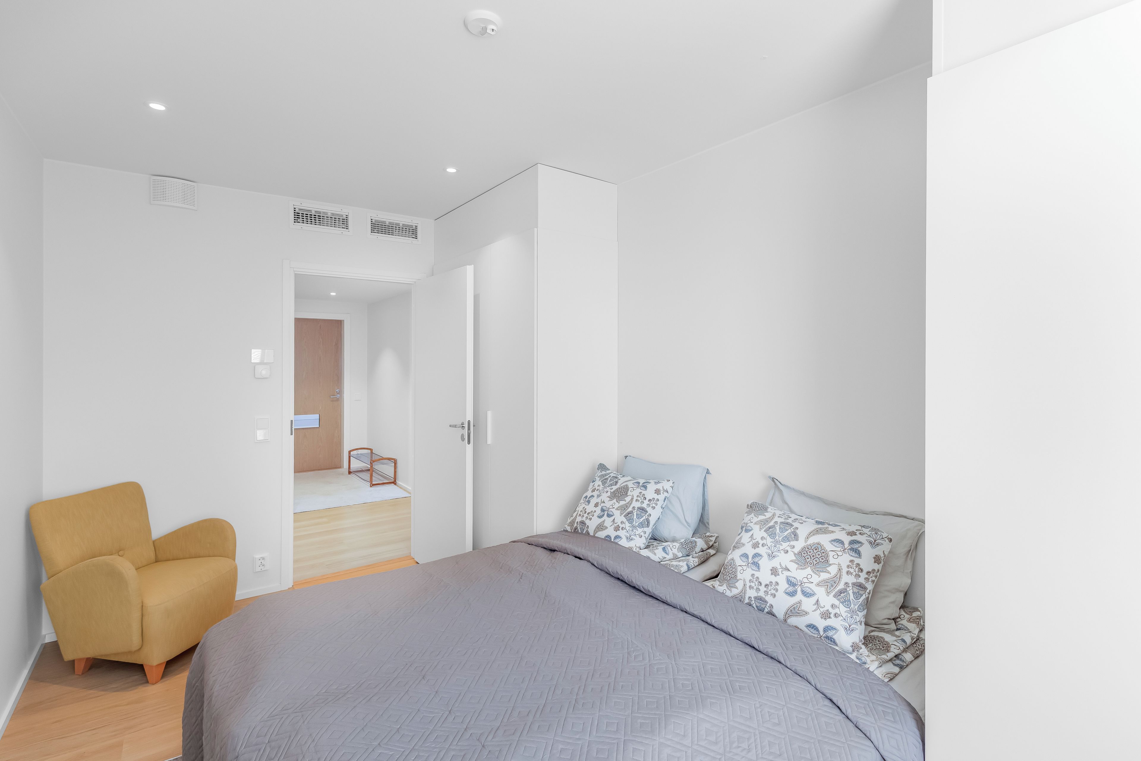 Une chambre à coucher moderne, avec un lit, une chaise et une porte donnant sur une autre pièce.