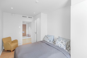 Un dormitorio moderno con una cama, una silla y una puerta que da a otra habitación.