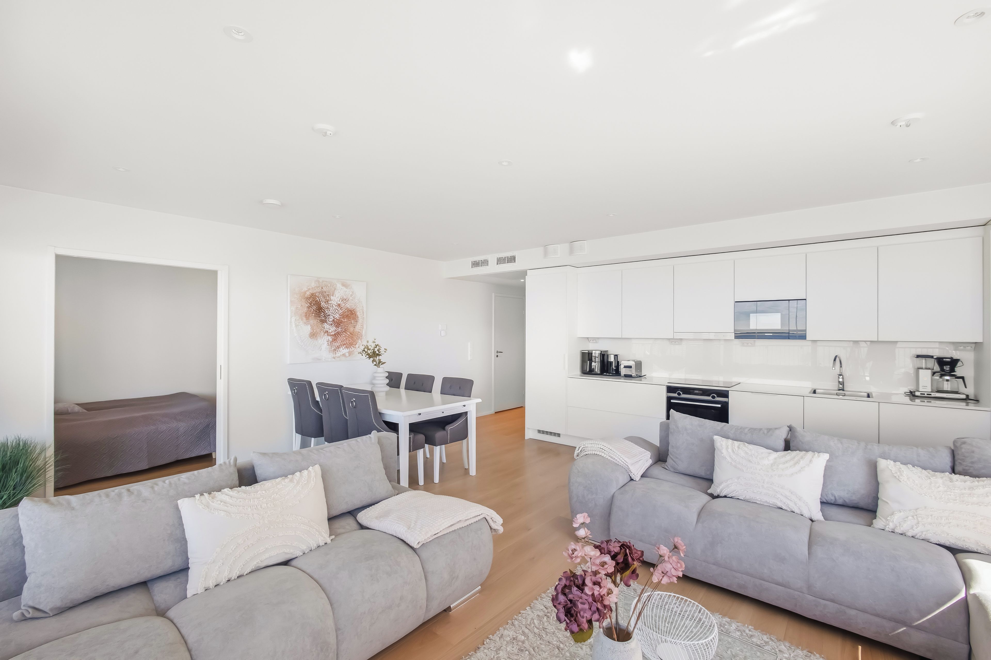 Un apartamento moderno con comedor, cocina y dos sofás grises con cojines blancos.