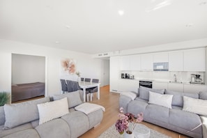 Un appartement moderne comprenant un coin repas, une cuisine et deux canapés gris avec des coussins blancs.