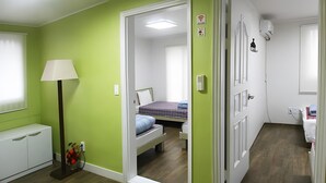 A room with green walls, a bed with a blue blanket, a bedside table, a lamp, and a mirror. - Seeu House (Seoul)