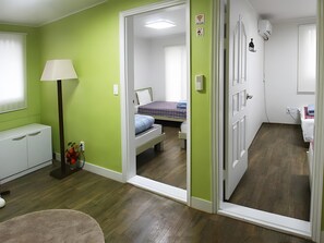A room with green walls, a bed with a blue blanket, a bedside table, a lamp, and a mirror. - Seeu House (Seoul)