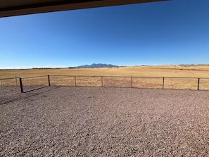 A gravel patio with a metal fence and a clear view of a mountainous landscape. - Ben's Place - A Quiet Sanctuary where you can enjoy sunrises and sunsets. (Sonoita)