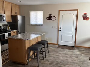 Eine Küche mit Holzschränken, einem Edelstahlkühlschrank, einer Granitarbeitsplatte und zwei Barhocker.