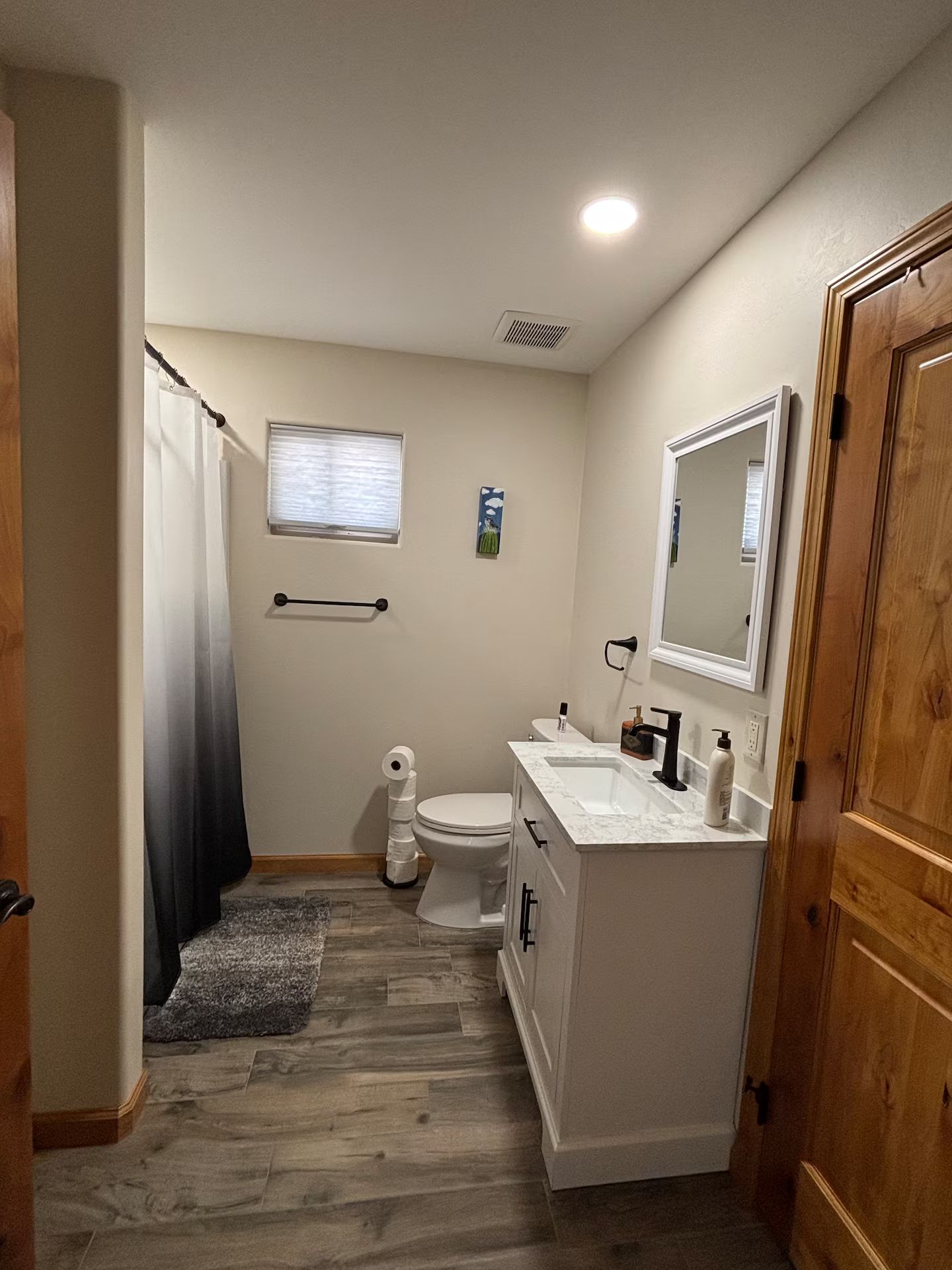 A bathroom with a toilet, sink, mirror, shower curtain, and a small window.
