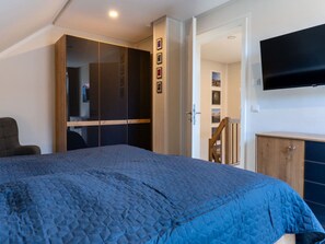 A bedroom with a bed, a wardrobe, a television, and a door leading to another room. - Holiday Home With 2 Bedrooms (Kellenhusen)