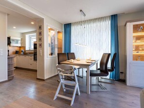 A modern dining area with a wooden table, two chairs, and a view of a kitchen and living space. - Holiday Home With 2 Bedrooms (Kellenhusen)