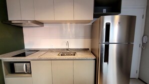 A compact kitchen with a built-in microwave, a stainless steel refrigerator, and a sink with a modern faucet. - Wire Capote Valente (São Paulo)