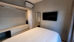 A modern hotel room with a bed, a built-in wardrobe, a TV mounted on the wall, and an air conditioning unit. - Wire Capote Valente (São Paulo)