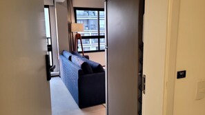 A hallway leading to a room with a sofa, a lamp, and a window with a view of buildings. - Wire Capote Valente (São Paulo)