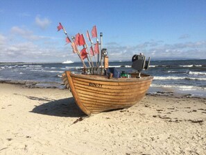Ein hölzernes Boot mit Flaggen an einem sandigen Strand, im Hintergrund der Ozean.