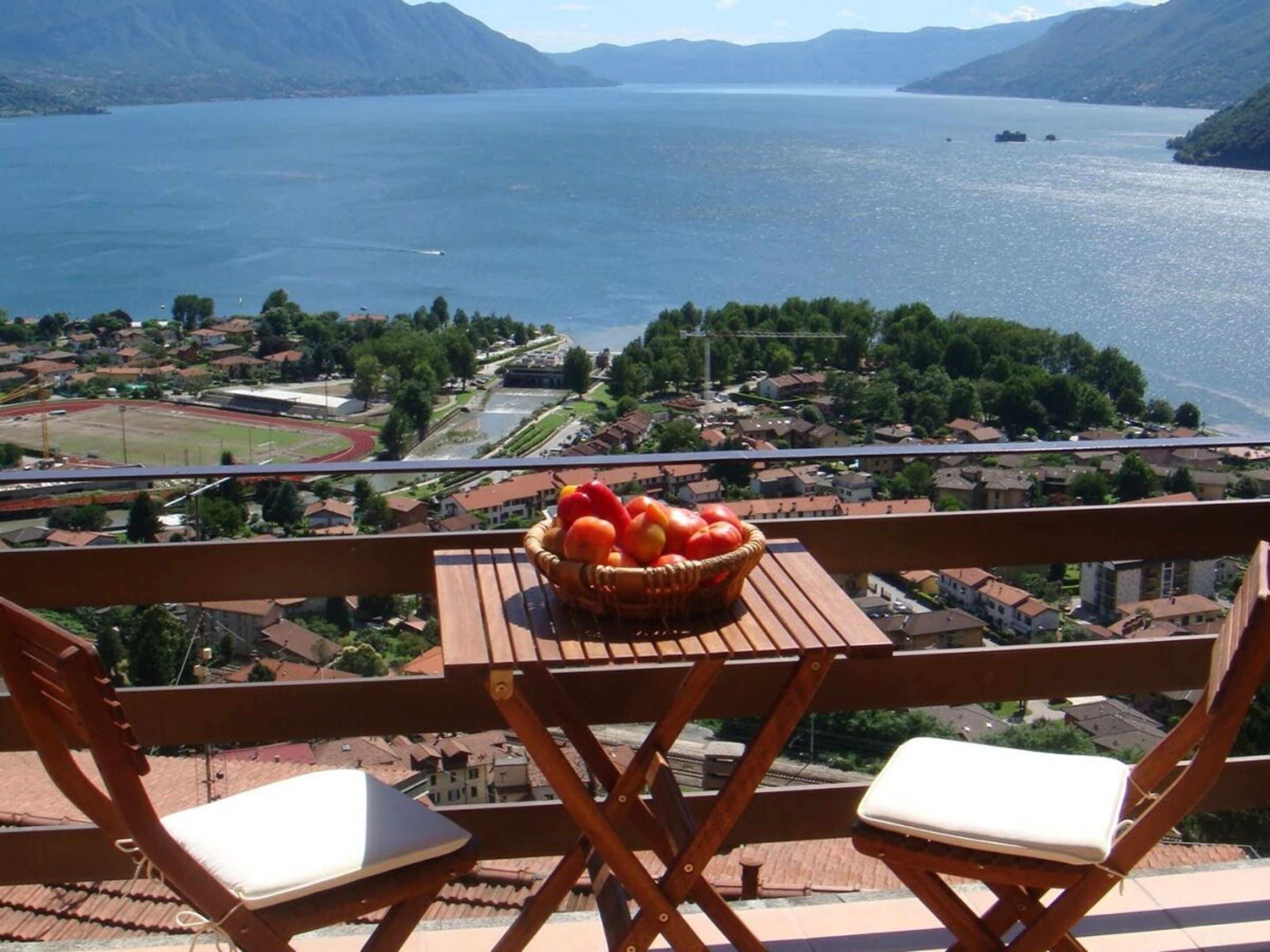 Un balcon donnant sur un lac, un panier de fruits et deux fauteuils confortables.
