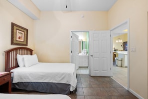 A bedroom with a bed, a nightstand, a framed picture on the wall, and a bathroom visible through an open door. - Windemere 405 (Pensacola)