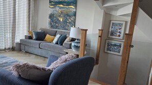 Ein Wohnzimmer mit grauem Sofa, blauem Sessel und einer Lampe auf einem Beistelltisch.