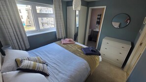 Ein Schlafzimmer mit einem Bett, einem Schminktisch, einem Spiegel und einem Fenster mit Vorhängen.