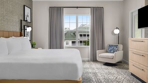 A hotel room with a large bed, a chair, a desk, a lamp, a TV, and a window with curtains. - Perfectly positioned within one of the top 25 destinations in the U.S. (Myrtle Beach)