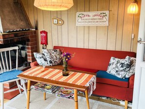 A cozy room with a red sofa, a wooden table with magazines, a small vase with flowers, and a wall clock. - 5 Person Holiday Home in Solvesborg (Sölvesborg)
