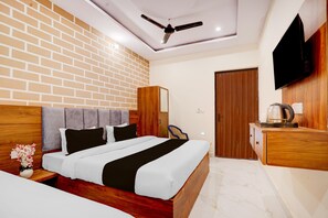 A hotel room with a brick-patterned wall, a bed with a wooden headboard, a ceiling fan, a wooden wardrobe, and a flat-screen TV mounted on the wall.