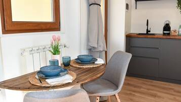 Een eethoek met een houten tafel, twee blauwe kommen, een vaas met roze bloemen en een grijze stoel.