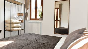 Ein Schlafzimmer mit Bett, Schrank, Heizkörper, einem Fenster mit Vorhängen und einem Spiegel.