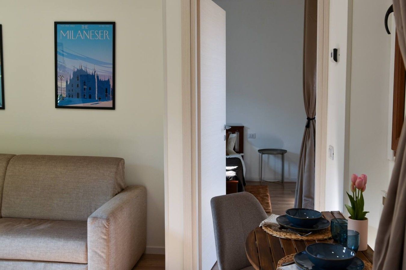 Un soggiorno con un divano, un tavolo da pranzo con piatti e un vaso di fiori, e un poster di un edificio appeso al muro.