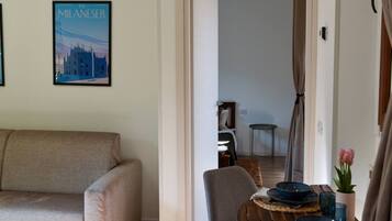 Un soggiorno con un divano, un tavolo da pranzo con piatti e un vaso di fiori, e un poster di un edificio appeso al muro.