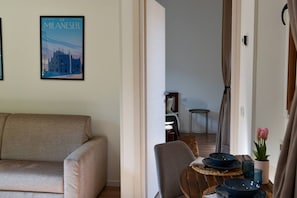 Un soggiorno con un divano, un tavolo da pranzo con piatti e un vaso di fiori, e un poster di un edificio appeso al muro.